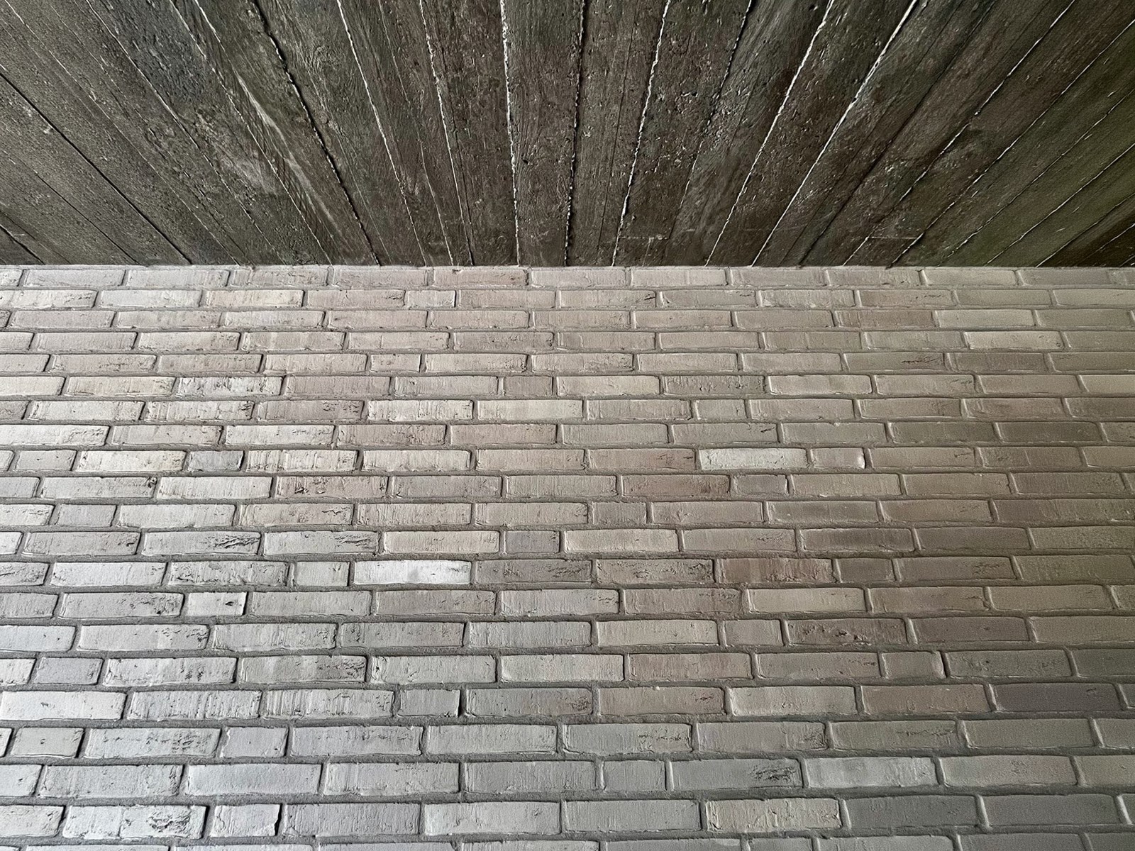 Architekturdetail — heller Klinker trifft auf eine Decke aus diagonal verlegten Holzdielen.